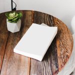 Libro blanco sobre mesa de madera junto a planta decorativa