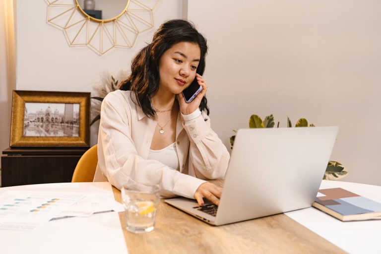 Mujer trabajando en su laptop mientras habla por teléfono.