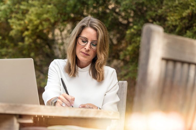 Mujer adulta escribiendo a mano junto a laptop en jardín