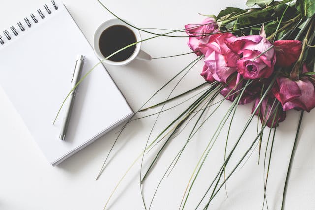 Cuaderno en blanco, bolígrafo, taza de café y ramo de rosas