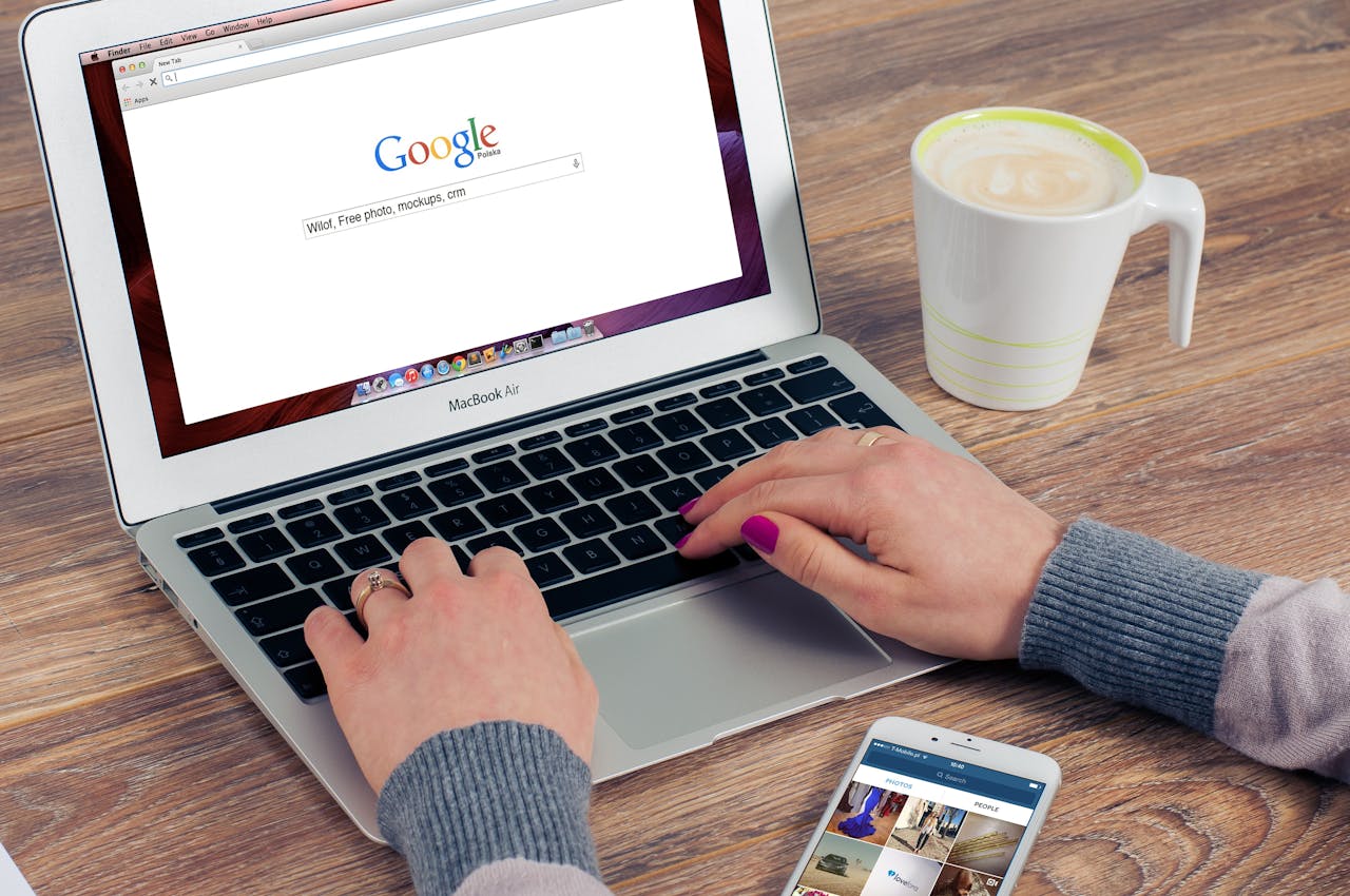 Persona escribiendo en Google desde su laptop con una taza de café al lado.