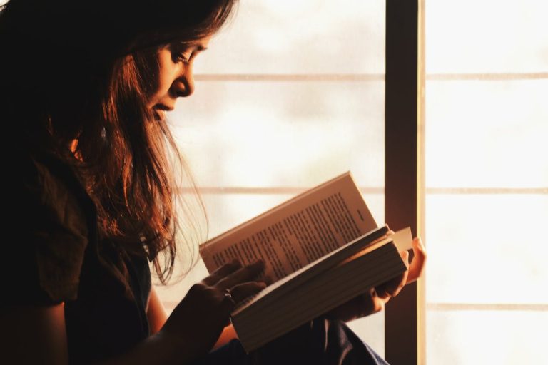 Mujer leyendo libro al atardecer junto a ventana
