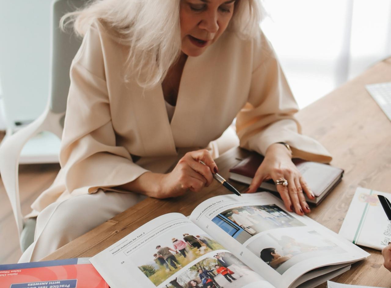 Mujer estudiando un libro de inglés con imágenes, acompañada en una sesión educativa personalizada.